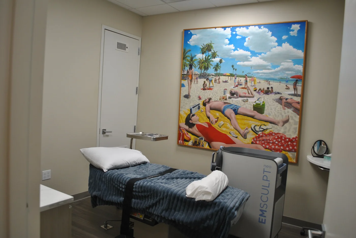 Empty treatment room with a reclining bed beneath framed beach artwork
