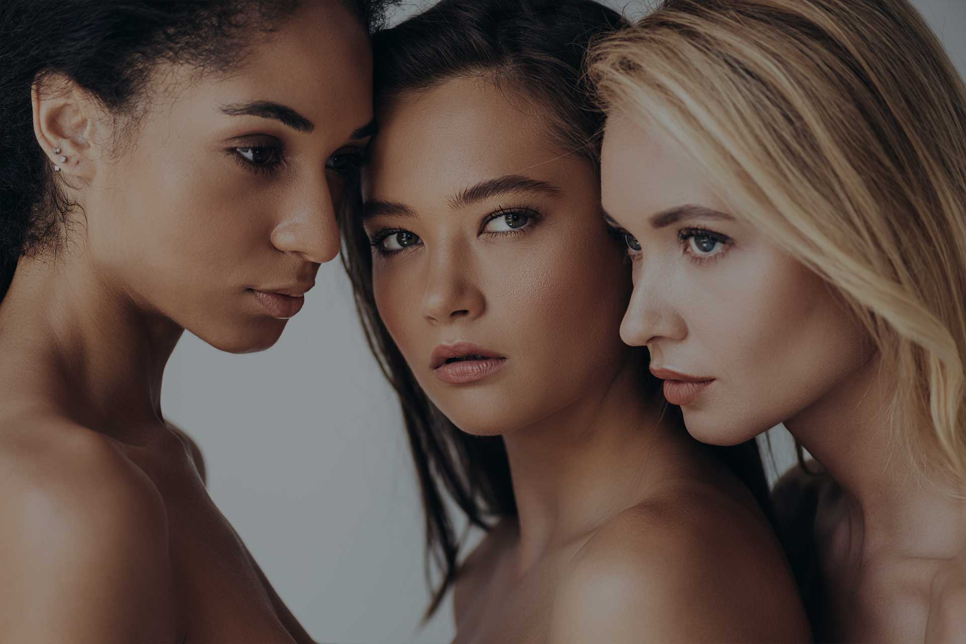 Three attractive multiethnic young women looking away isolated on grey